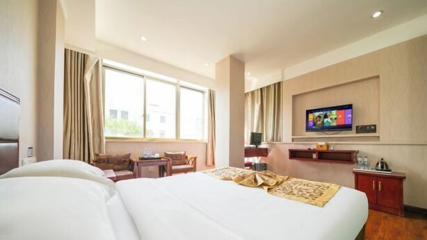 A hotel room with a large bed, a TV mounted on the wall, a desk, and a chair. - Changtai Hezheng Business Hotel (Zhangzhou)
