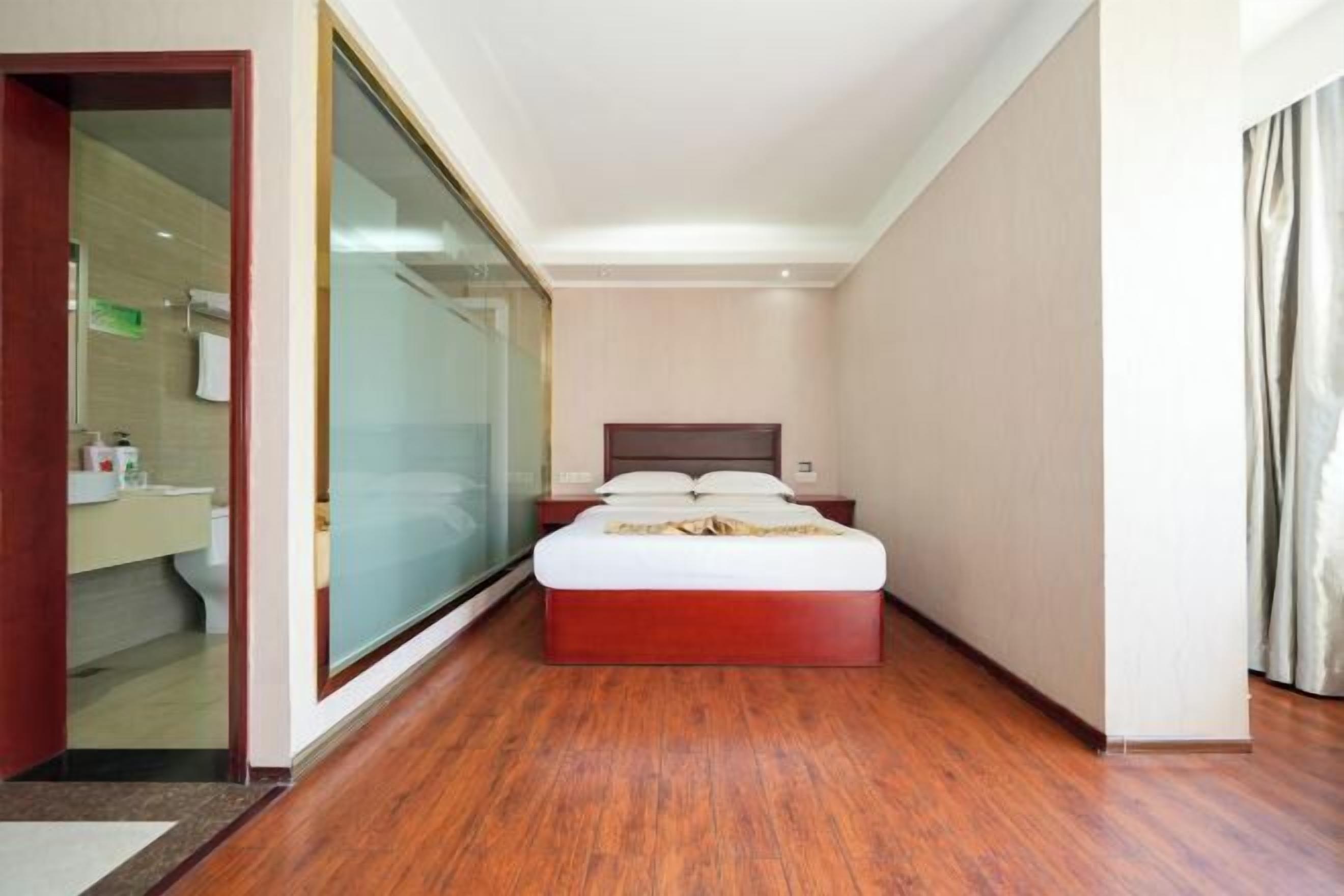 Een hotelkamer met een houten vloer, een bed met een houten hoofdeinde, een douchecabine van glas en uitzicht op de badkamer.