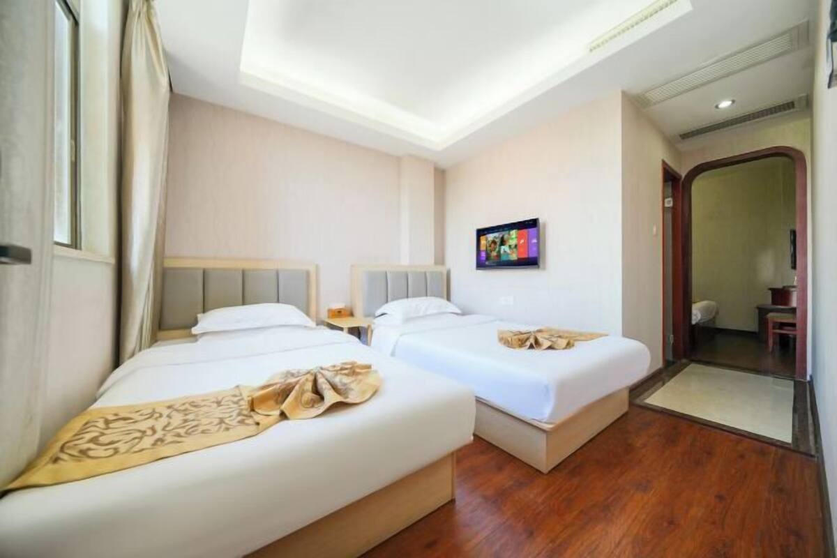 A hotel room with two beds, a flat-screen TV, and a wooden floor.