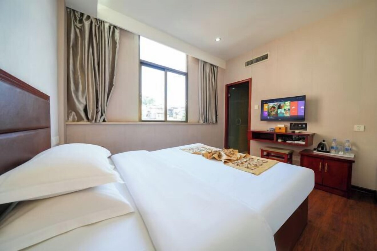 A hotel room with a bed, a television, a desk with a computer, and a window with curtains.