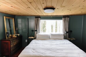 A bedroom with a wooden ceiling, a large bed, two bedside tables with lamps, a dresser, and a window with curtains. - 2 CABINS, 3 ACRES- HOT TUB VIEWS & ACCESS TO THE STATE PARK TRAILS  (Clayton)