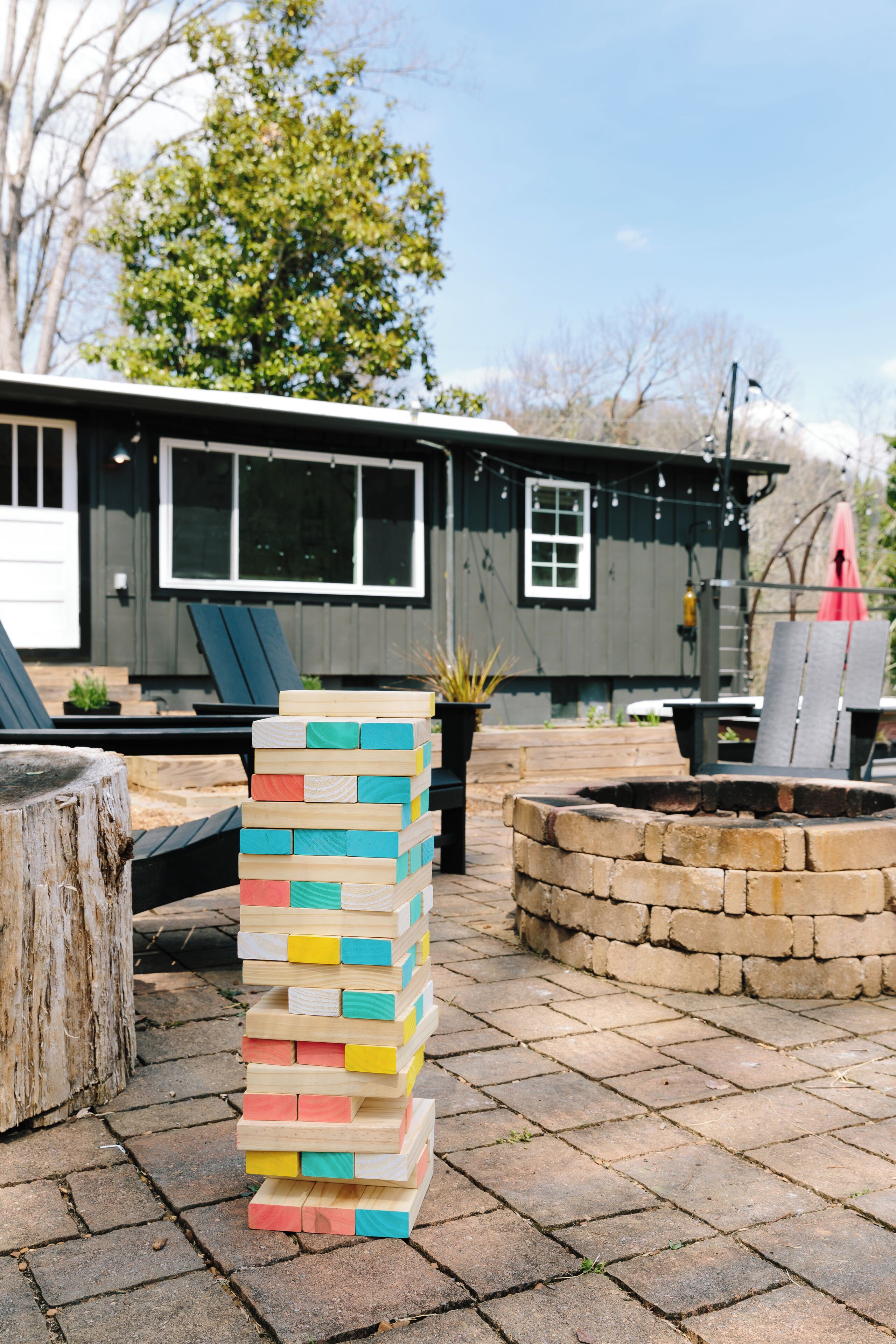 A stack of colorful wooden blocks outdoors, a stone fire pit, and a house with a deck and outdoor furniture.