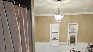 Ein Badezimmer mit Badewanne, Holzboden, einer Duschvorhang, einem Kronleuchter und einem kleinen Fenster mit Regalen.