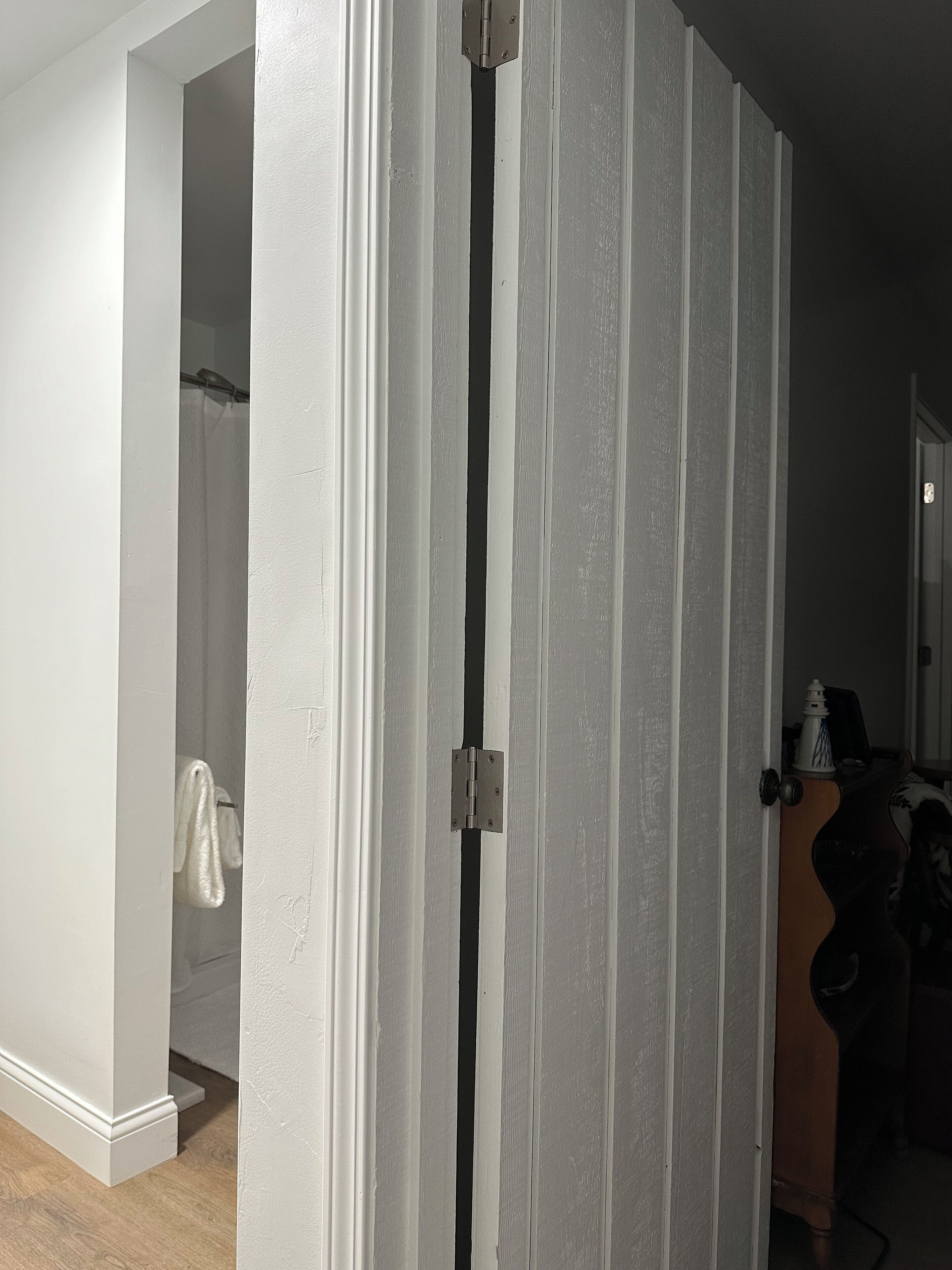 Une pièce dont la porte est entrouverte, laissant entrevoir une salle de bain où une serviette est accrochée au mur.