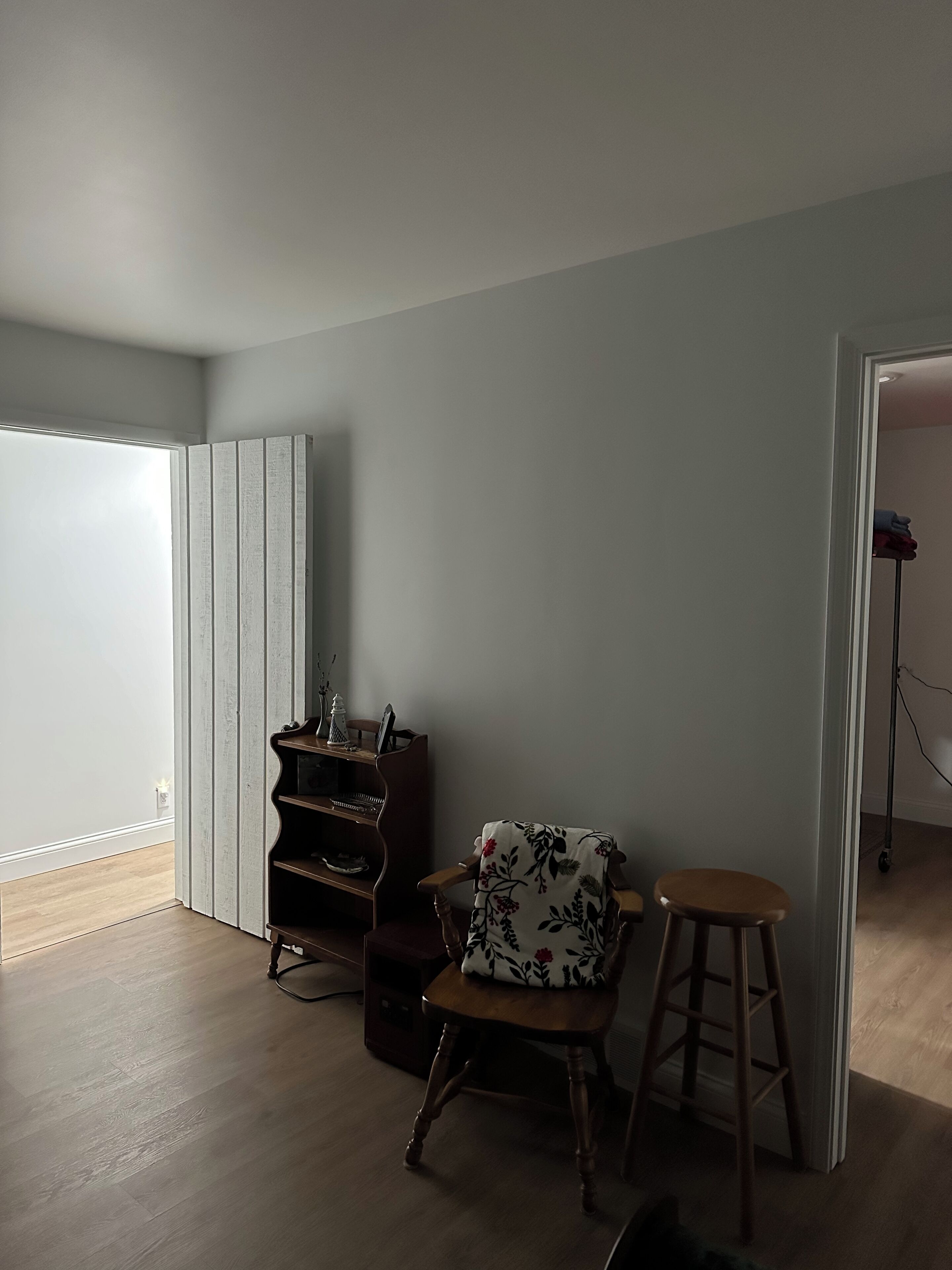 A room with a wooden floor, a wooden chair with a floral cushion, a small wooden table, and a wooden bookshelf.