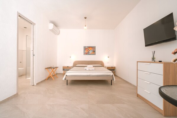 A modern bedroom with a bed, bedside tables, a TV, and a small desk.