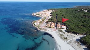 An aerial view of a coastal town with a beach, a red flag, and a mix of residential buildings.
