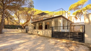 A modern house with a covered patio, gravel driveway, and a gated entrance.