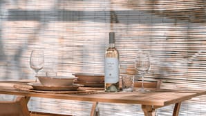 A wooden table set with plates, bowls, a wine bottle, and glasses.