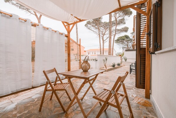 An outdoor patio with a stone floor, wooden furniture, and a white canopy. - Domus Lucia 4 (Santa Lucia)