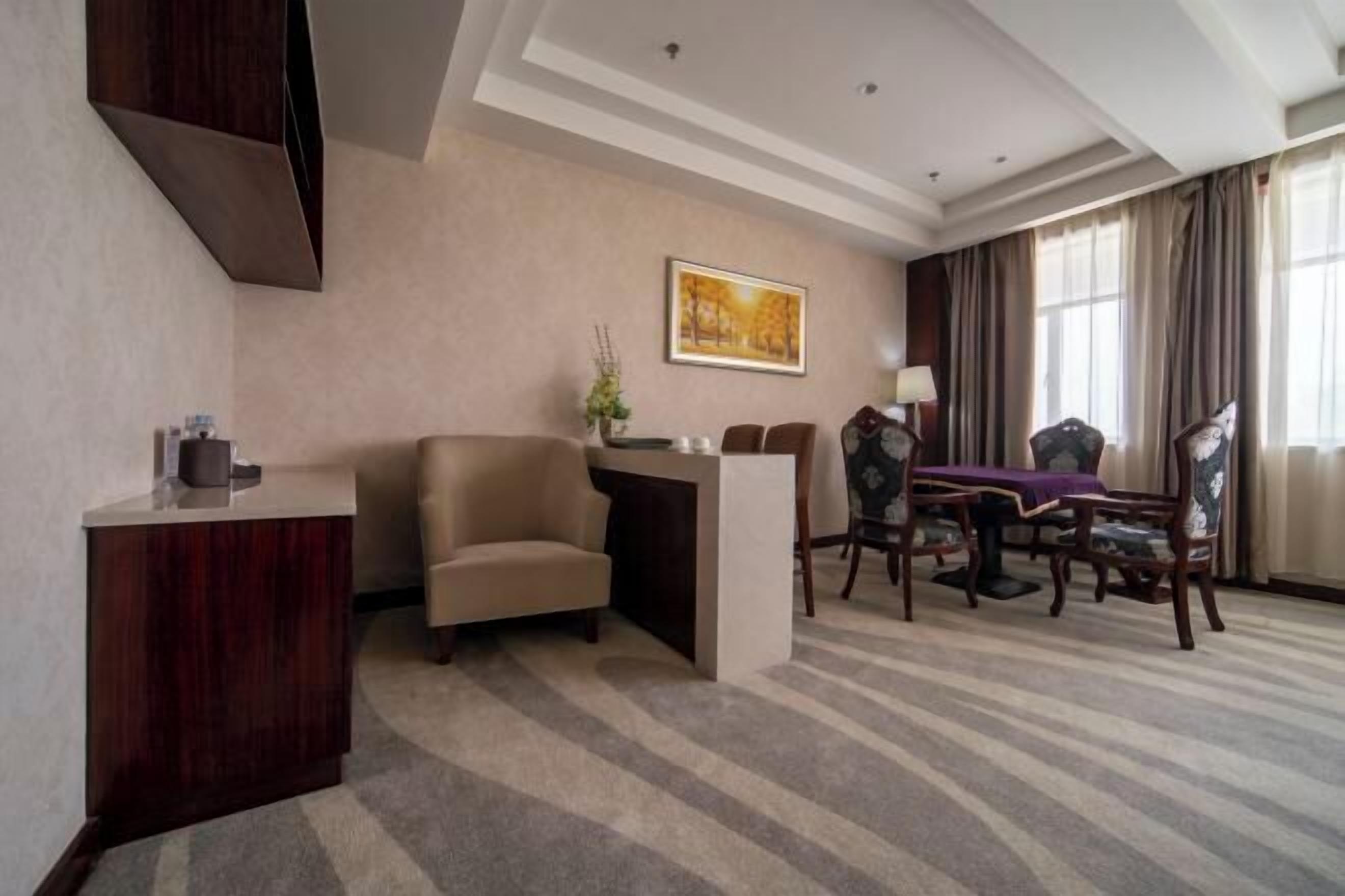 A hotel room with a dining area, a sofa, a desk, and a painting on the wall.
