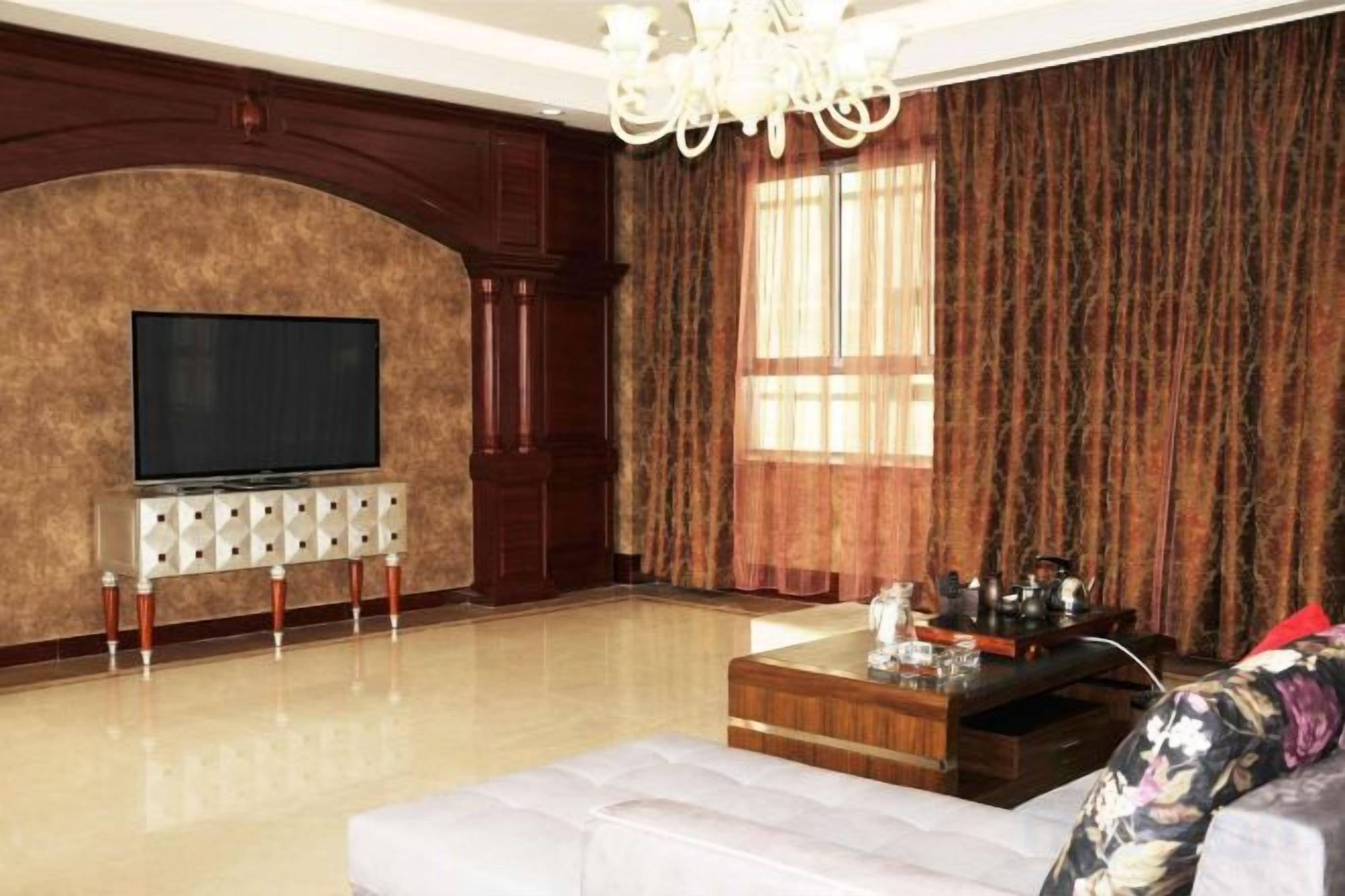 A living room with a flat-screen TV on a stand, a sofa, a coffee table, and a chandelier.