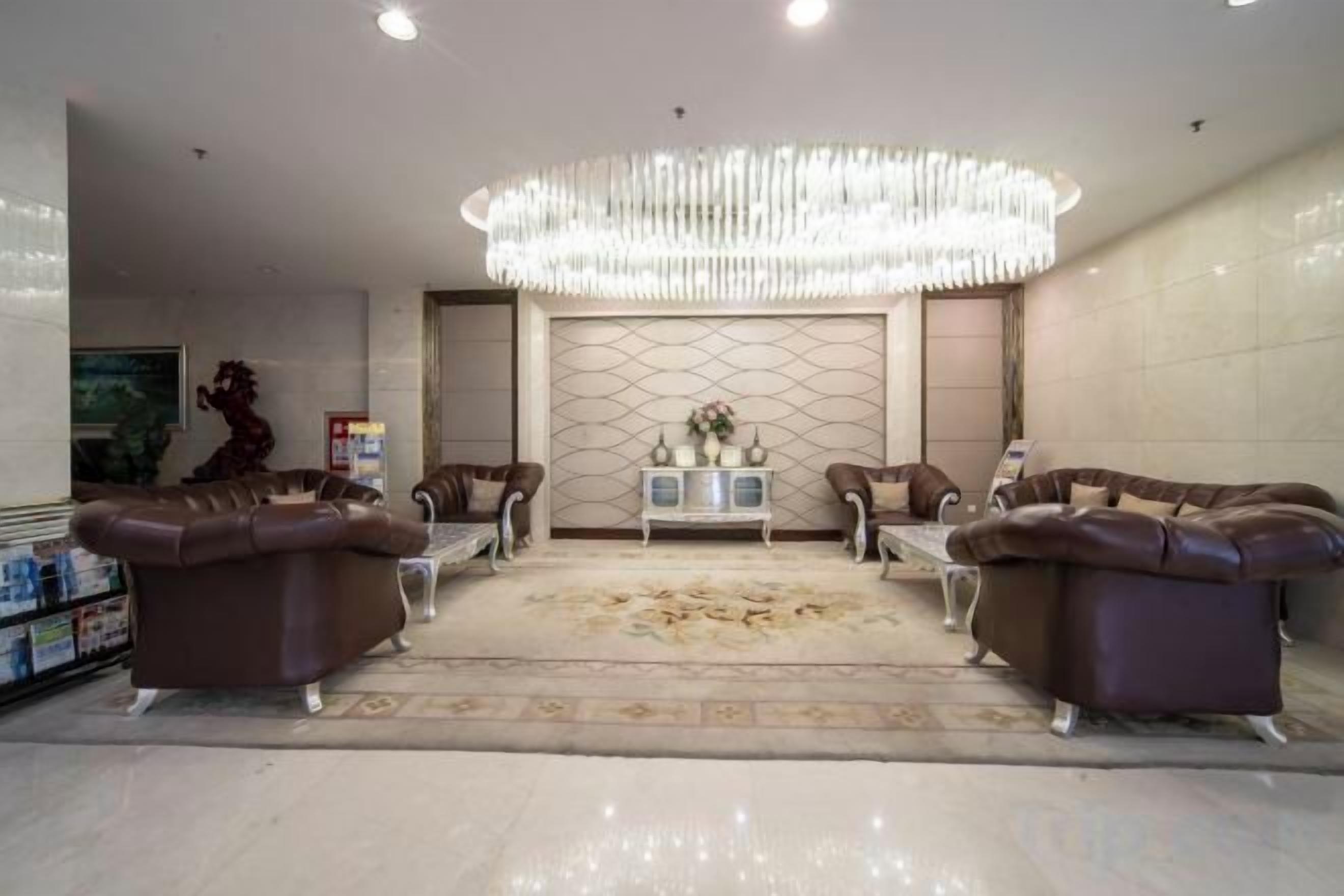 A spacious living area with a large chandelier, leather sofas, a coffee table, and a decorative rug.