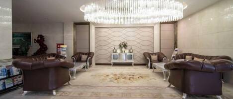 A spacious living area with a large chandelier, leather sofas, a coffee table, and a decorative rug.