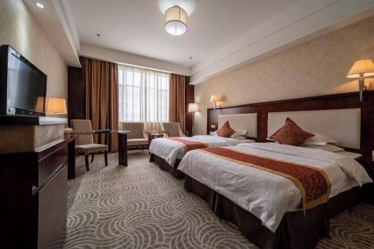 A hotel room with two beds, a TV, a desk, and a chair.
