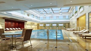 A spacious indoor swimming pool with a glass ceiling, lounge chairs, and a seating area with tables. - Western Regions Spring Hotel (Wensu)