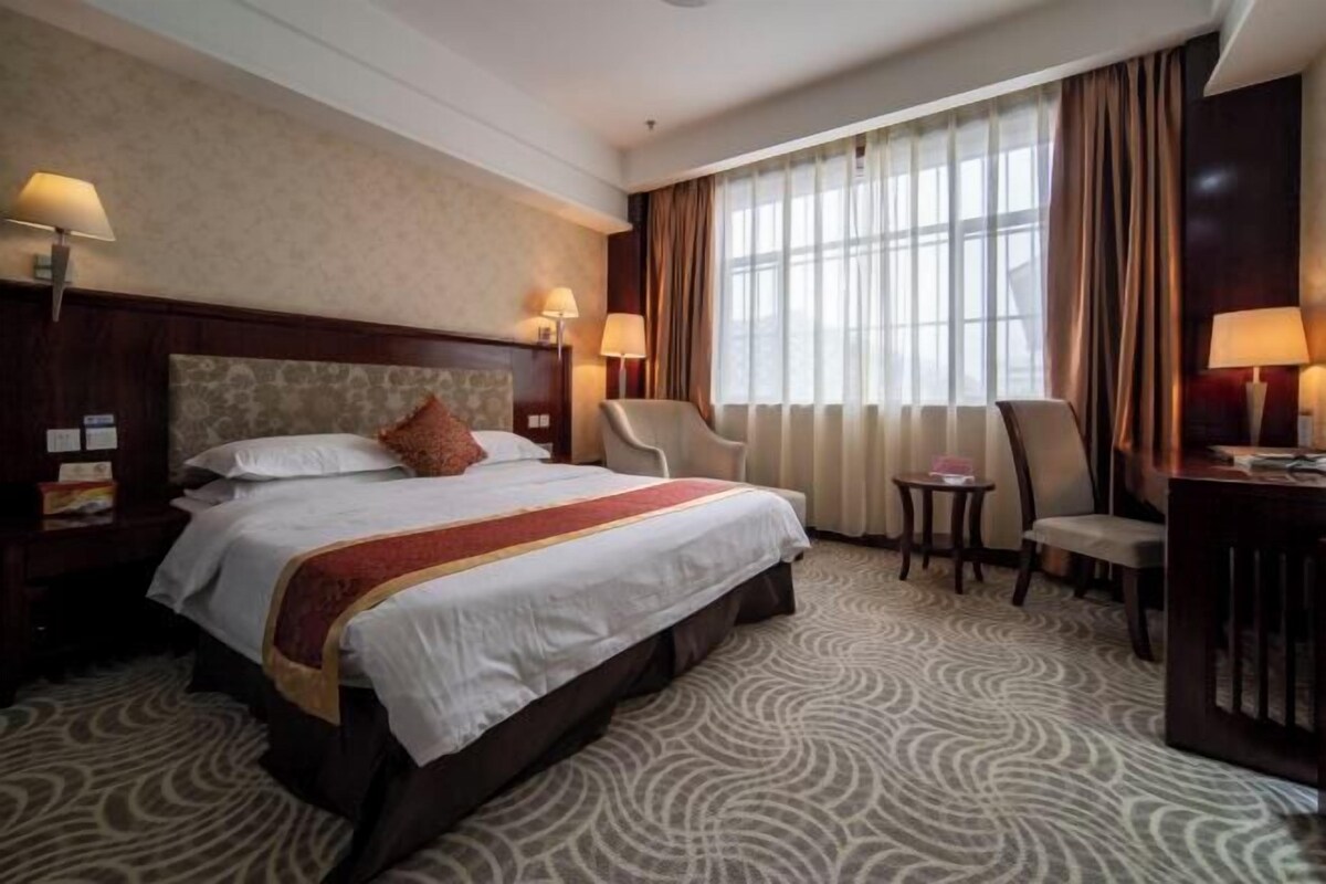 Een hotelkamer met een groot bed, twee bedlampen, een klein tafeltje, een stoel en een bureau met een lamp.