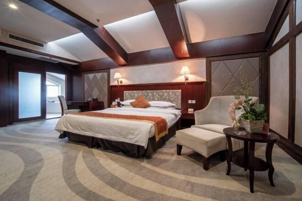 A hotel room with a large bed, a chair, a small table with a plant, and a decorative wall panel.