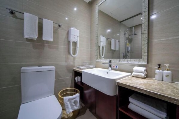 Een moderne badkamer met toilet, wastafel en spiegel. Handdoeken hangen aan de muur en er staat een mand met handdoeken op de vloer.