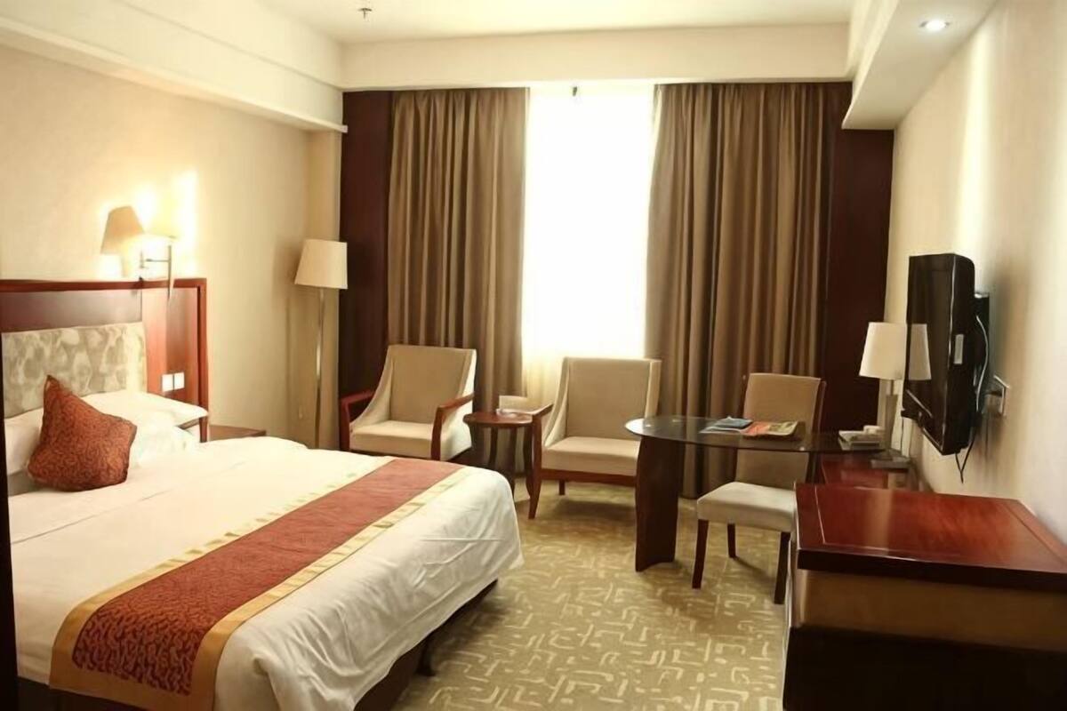 A hotel room with a bed, two chairs, a small table, a TV, and a window with curtains.