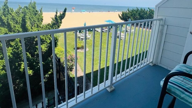 Een balkon met uitzicht op een strand, een gazon en enkele parasols.