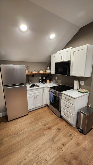 A modern kitchen with white cabinetry, stainless steel appliances, and a wooden floor. - "The Nest" is a unique hideaway in the woods with convenient access. (Titusville)