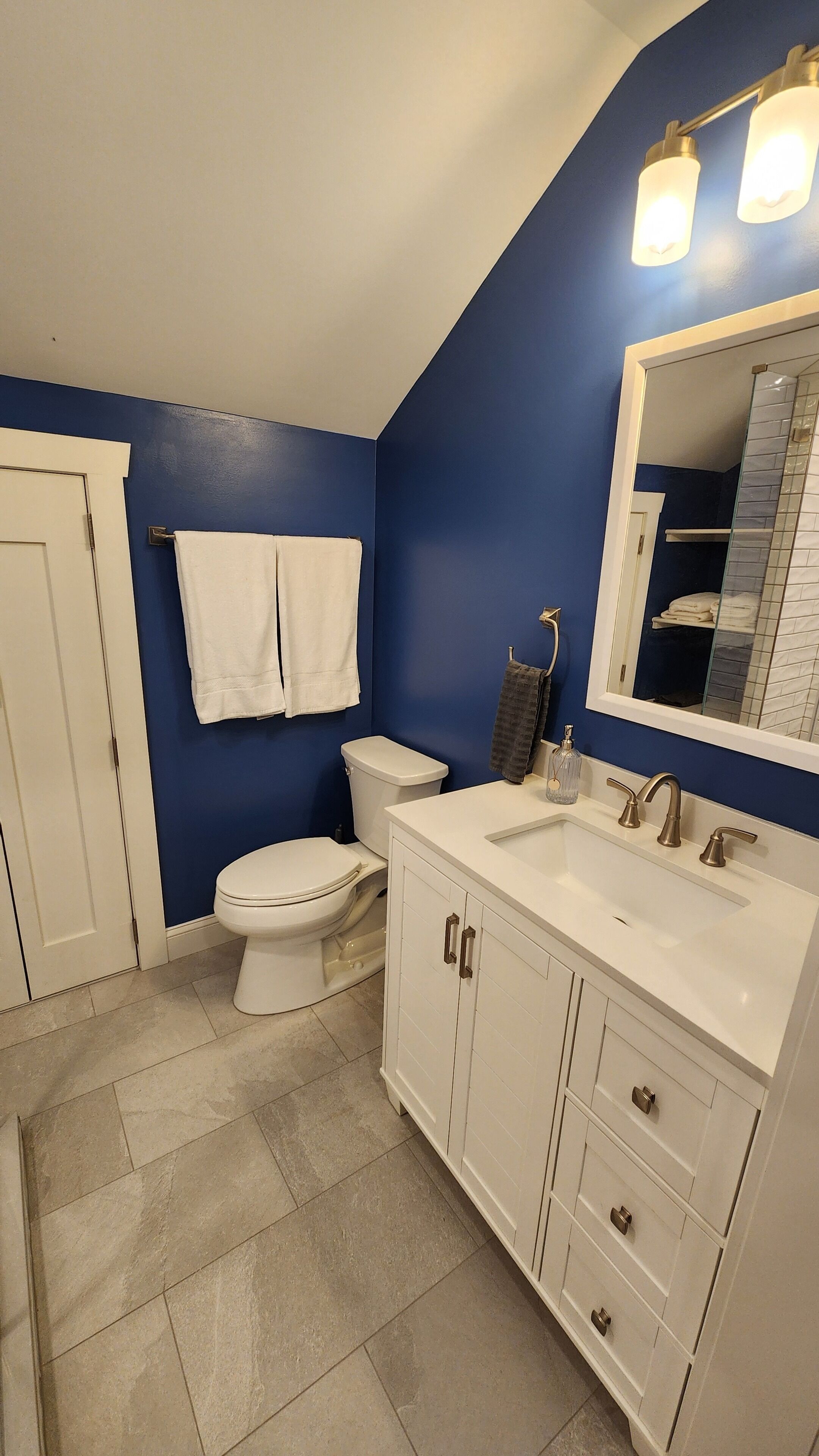A bathroom with a white toilet, a white sink with a mirror above it, and a blue wall.