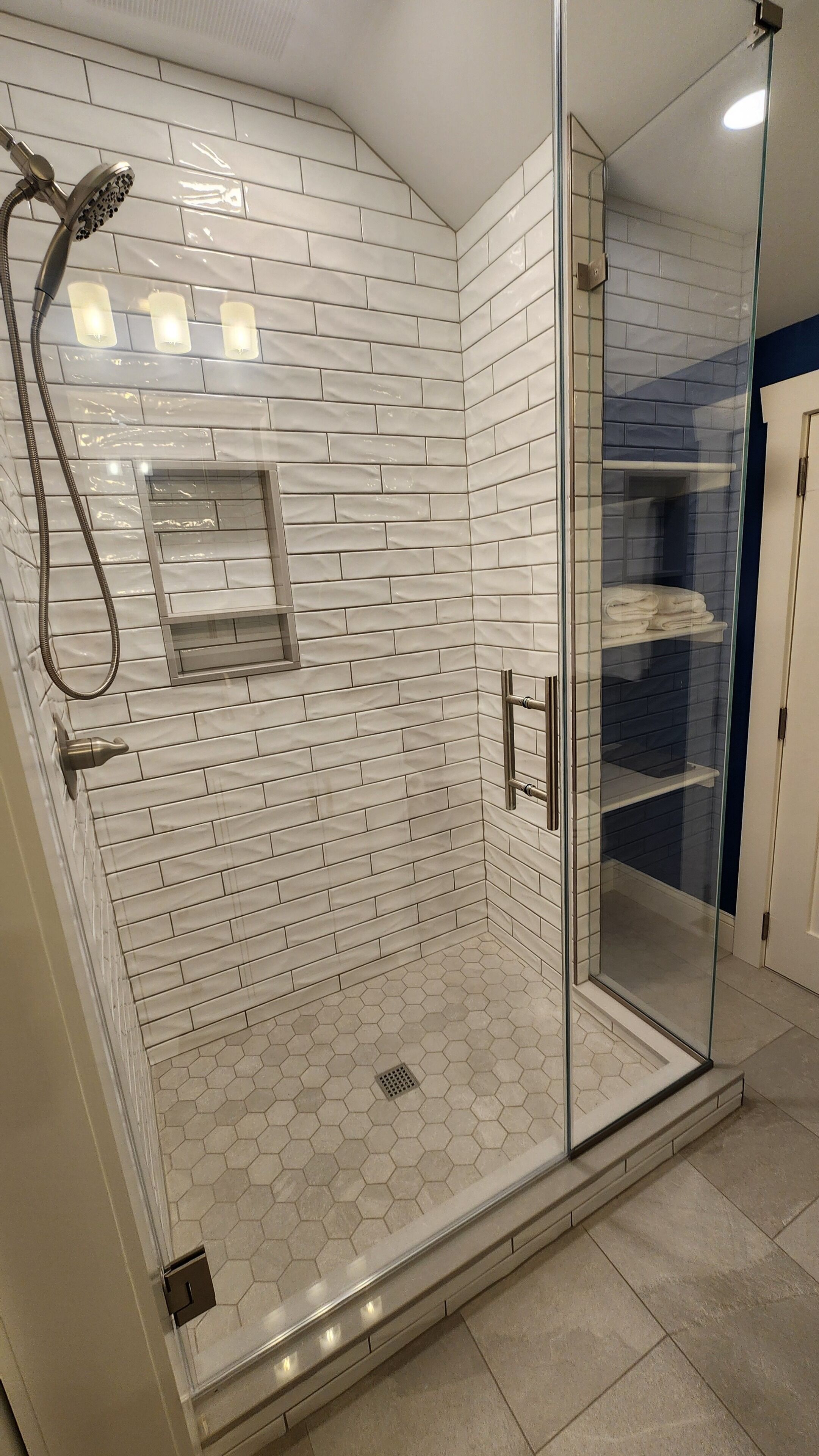 Ducha con cerramiento de vidrio, azulejos blancos tipo metro y suelo de baldosas hexagonales.