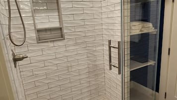 Ducha con cerramiento de vidrio, azulejos blancos tipo metro y suelo de baldosas hexagonales.