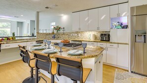 A modern kitchen with white cabinets, a granite countertop, and a central island with bar stools. - Exquisite Canal-Front Home: Access to Lake Conroe! (Montgomery)
