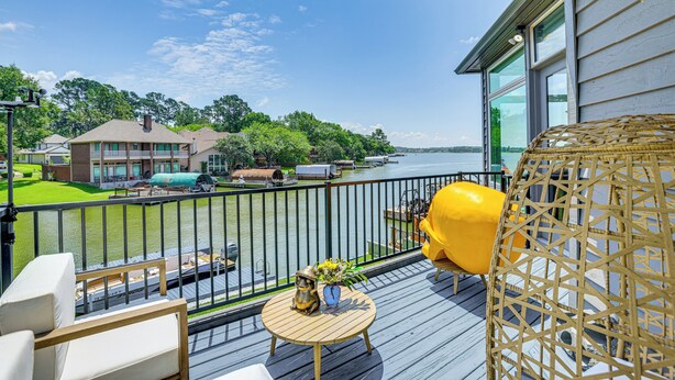 A deck with outdoor furniture, a yellow chair, and a view of a lake and buildings. - Exquisite Canal-Front Home: Access to Lake Conroe! (Montgomery)