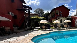 A swimming pool with stone tiles, lounge chairs, and umbrellas. - Pousada Villa Zen (Pirenópolis)