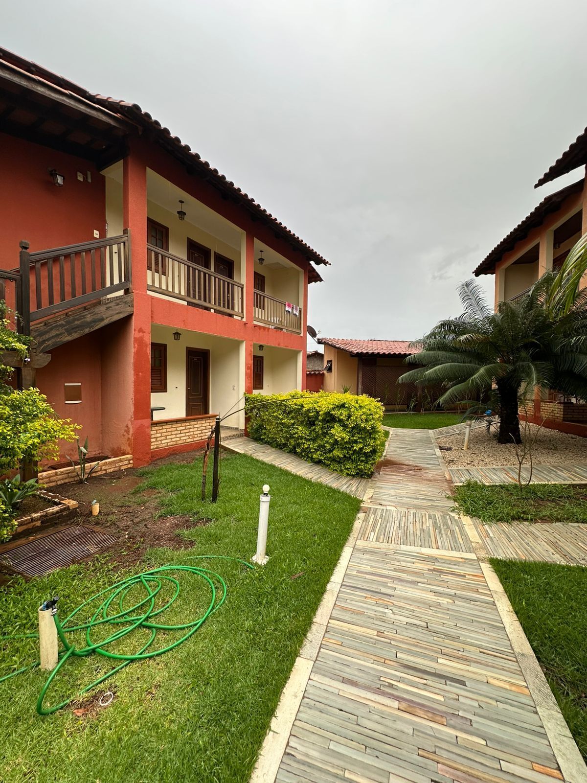 A courtyard with a wooden pathway, a small garden, and a two-story building with balconies.