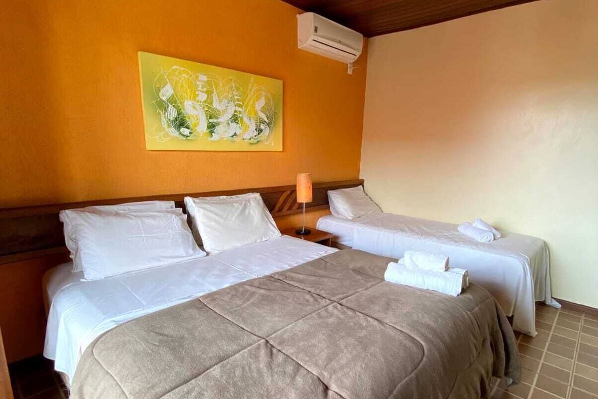 A hotel room with two beds, a wooden ceiling, a painting on the wall, and an air conditioning unit.
