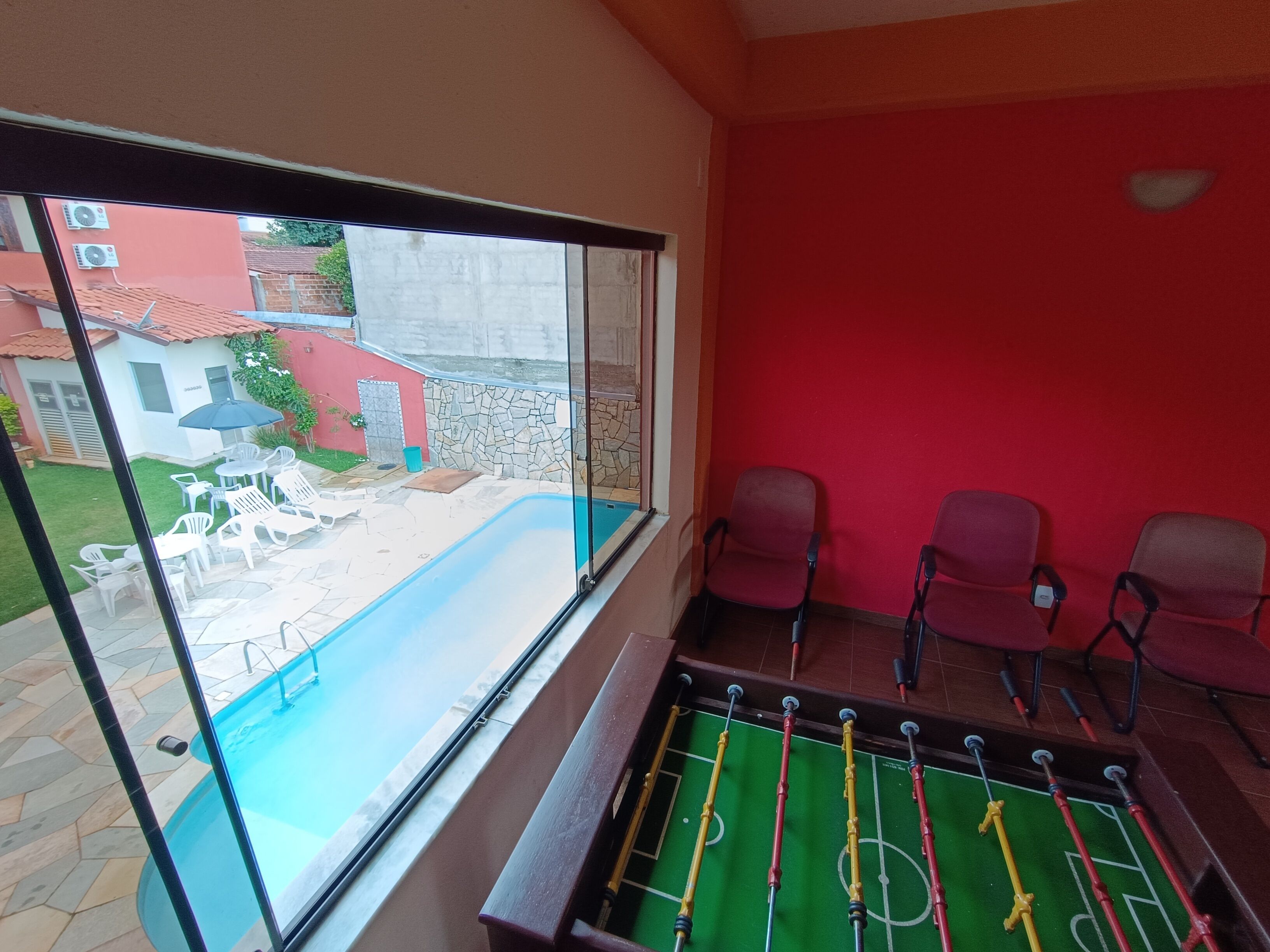 Une pièce dotée d’un mur de verre donnant sur une piscine et un espace extérieur aménagé pour se détendre.