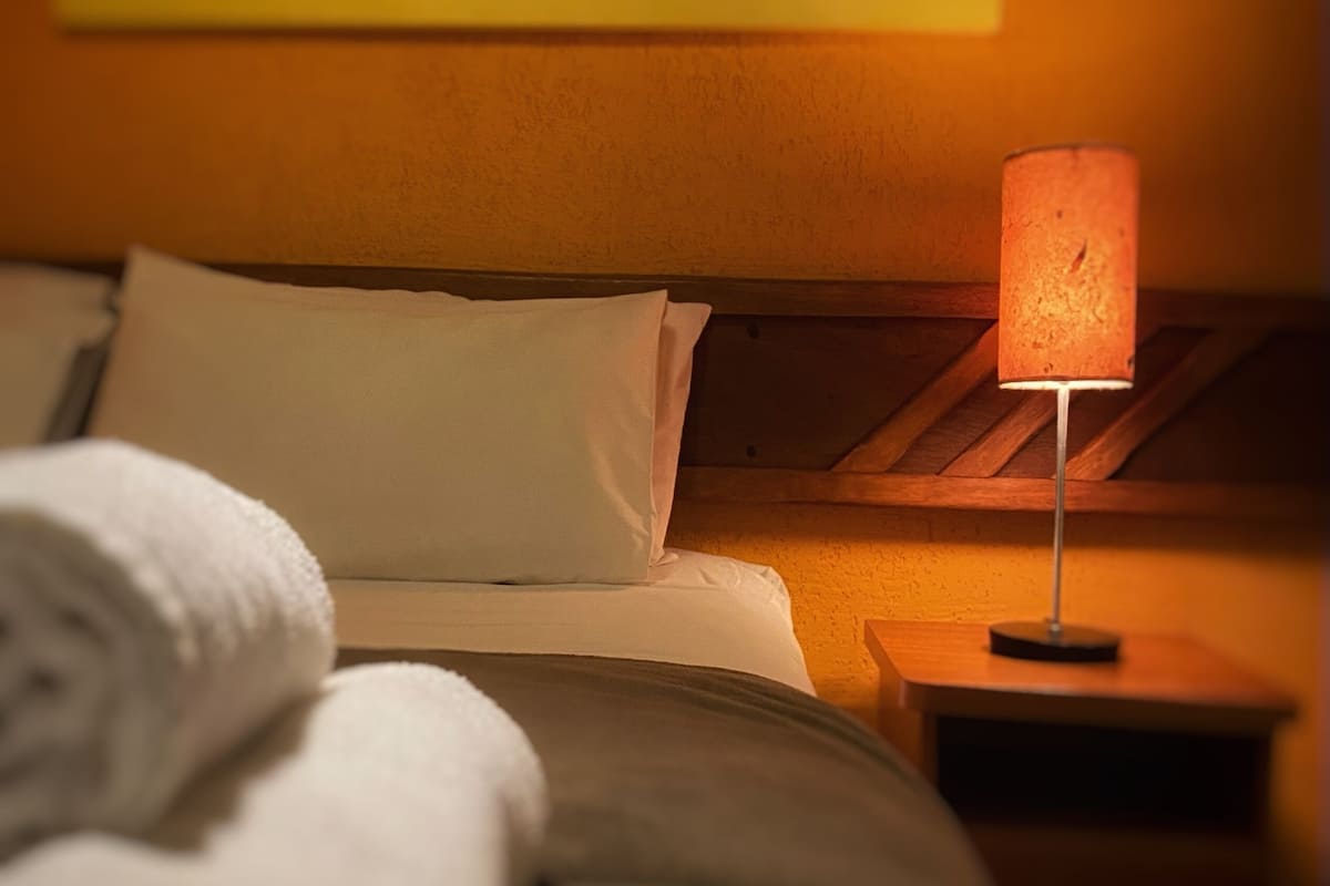 A neatly made bed with white linens, a wooden headboard, and a bedside table with a lamp.