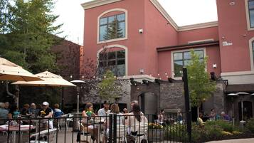 An outdoor patio area with tables and chairs, surrounded by a stone wall and a building with large windows and a brick facade.