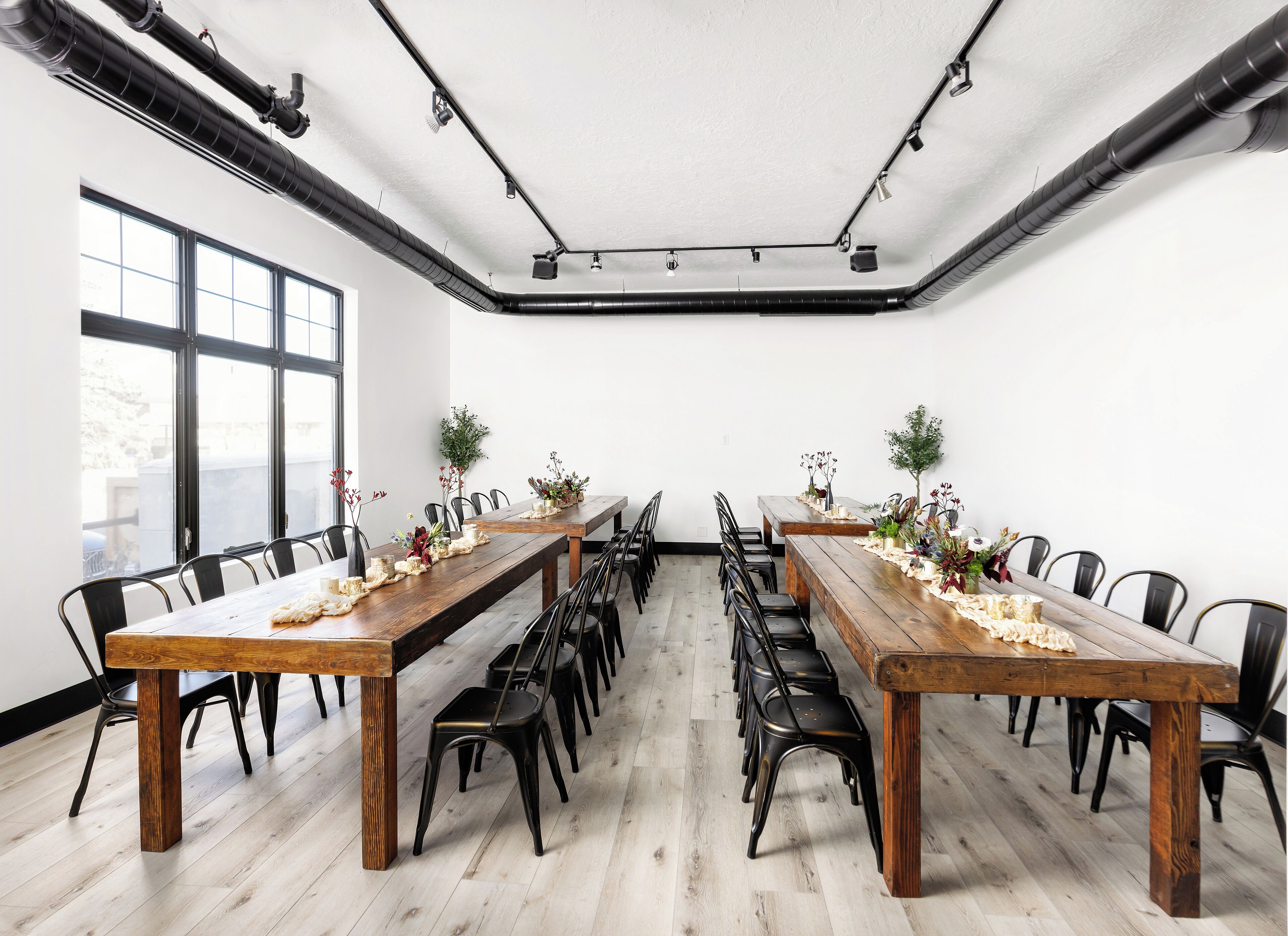 Un salón de conferencias con dos largas mesas de madera, sillas negras y plantas en macetas.