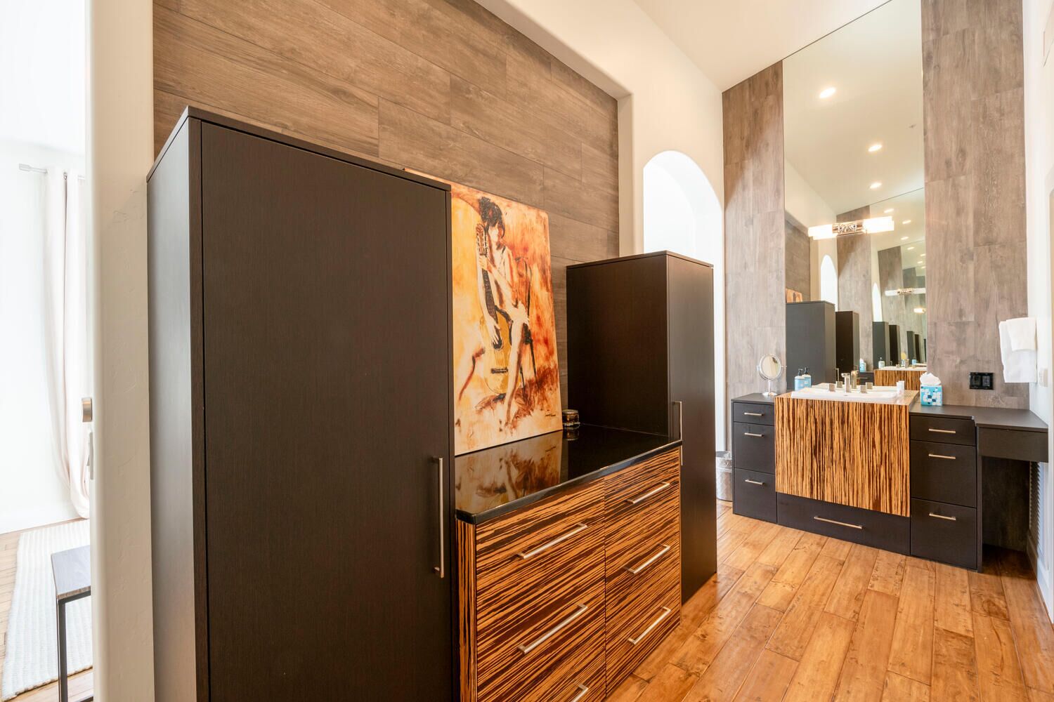 A modern bathroom with a wooden vanity, a large mirror, and a painting on the wall.