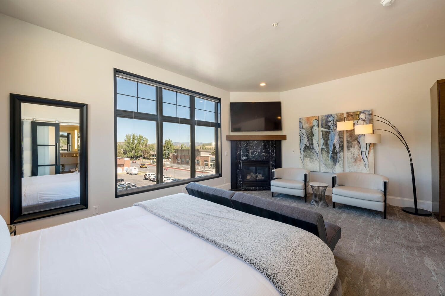 Una habitación de hotel moderna con una cama grande, chimenea, televisor y vistas al exterior.