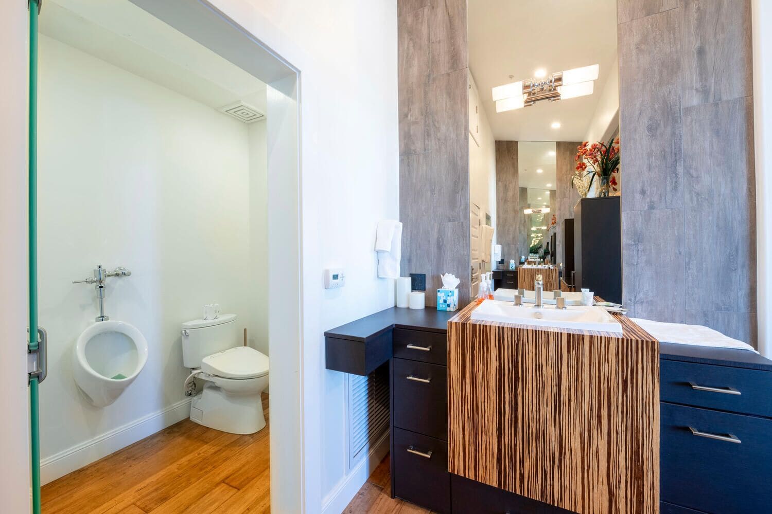 Un baño moderno con tocador de madera, inodoro y orinal.