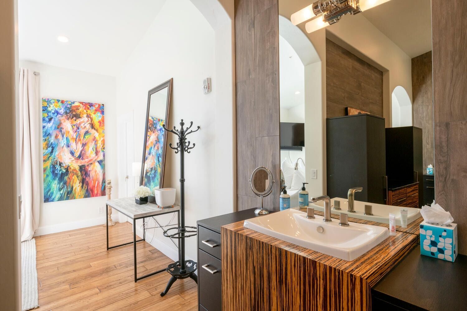 Un baño moderno con un espejo grande, un tocador de madera y un cuadro abstracto colorido en la pared.
