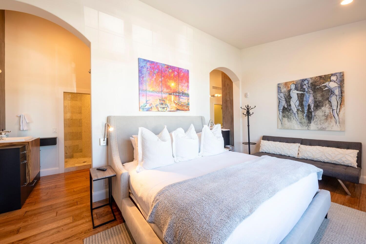 Een moderne hotelkamer met een groot bed, een nachtkastje, een bureau en een stoel. Er hangt een schilderij aan de muur en staat een kapstok.
