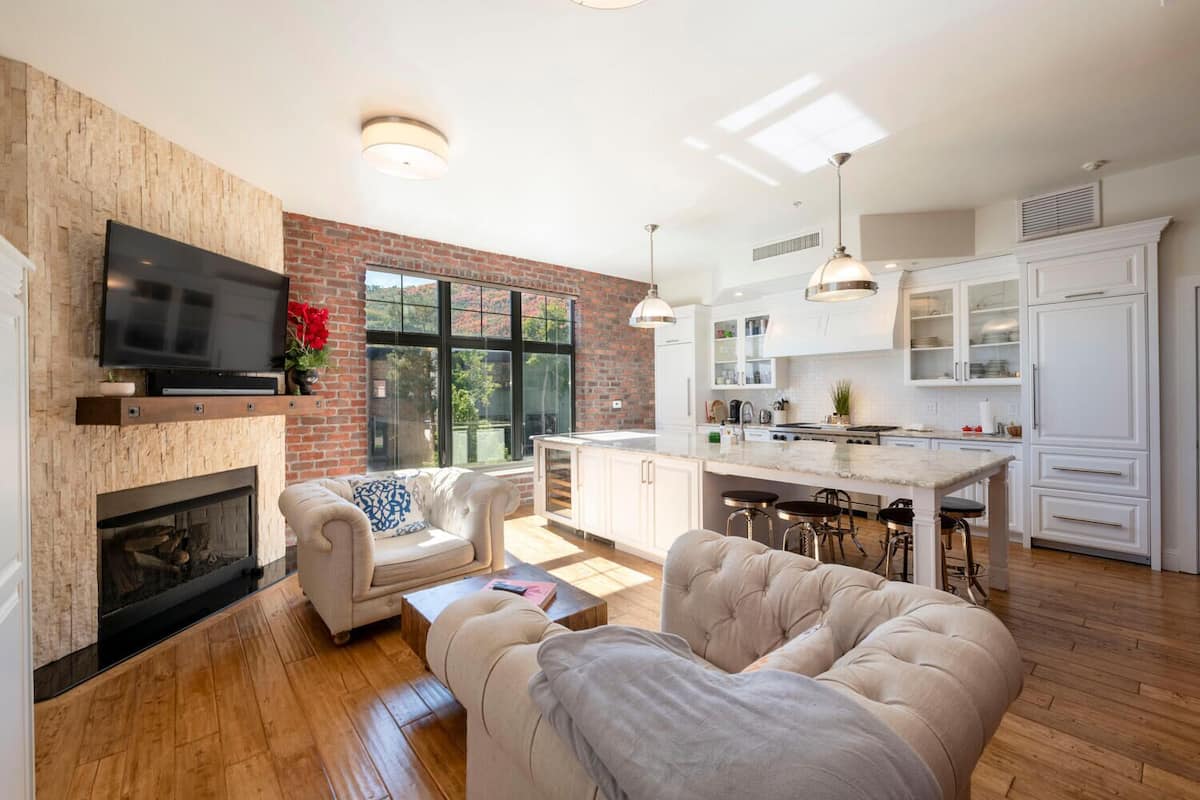A modern living room with a fireplace, a television, and a kitchen with white cabinets and a bar area.