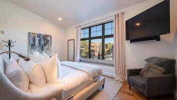 Un dormitorio moderno con una cama grande, un sillón gris, un televisor de pantalla plana y un ventanal con vistas al exterior.