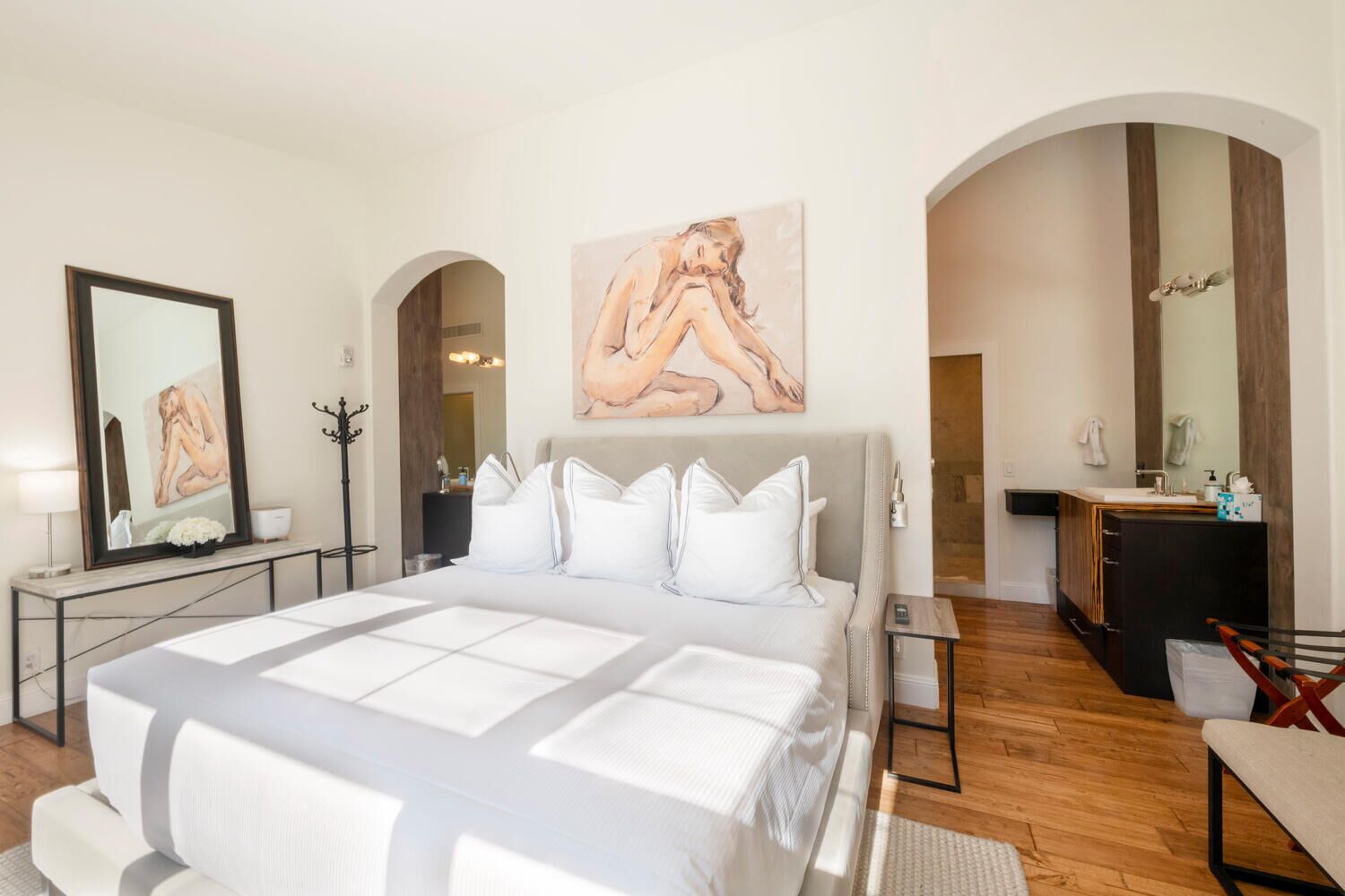 Um quarto moderno com uma cama grande, uma toucador com espelho e um quadro na parede.