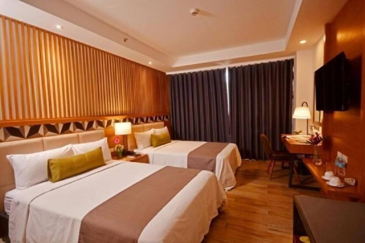 Ein Hotelzimmer mit zwei Betten, einem Schreibtisch, einem Stuhl, einem Fernseher und einem Vorhang.