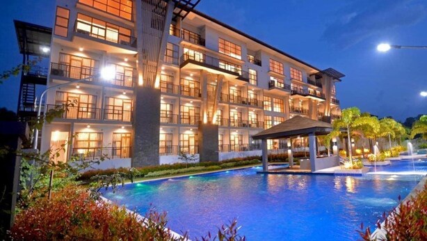 A multi-story hotel with a swimming pool and outdoor lighting. - Crown Hotel Palawan at Harbour Springs (Puerto Princesa)