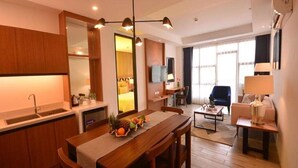 A modern hotel room with a wooden dining table, kitchen area, and a living space with a sofa and armchair. - Crown Hotel Palawan at Harbour Springs (Puerto Princesa)