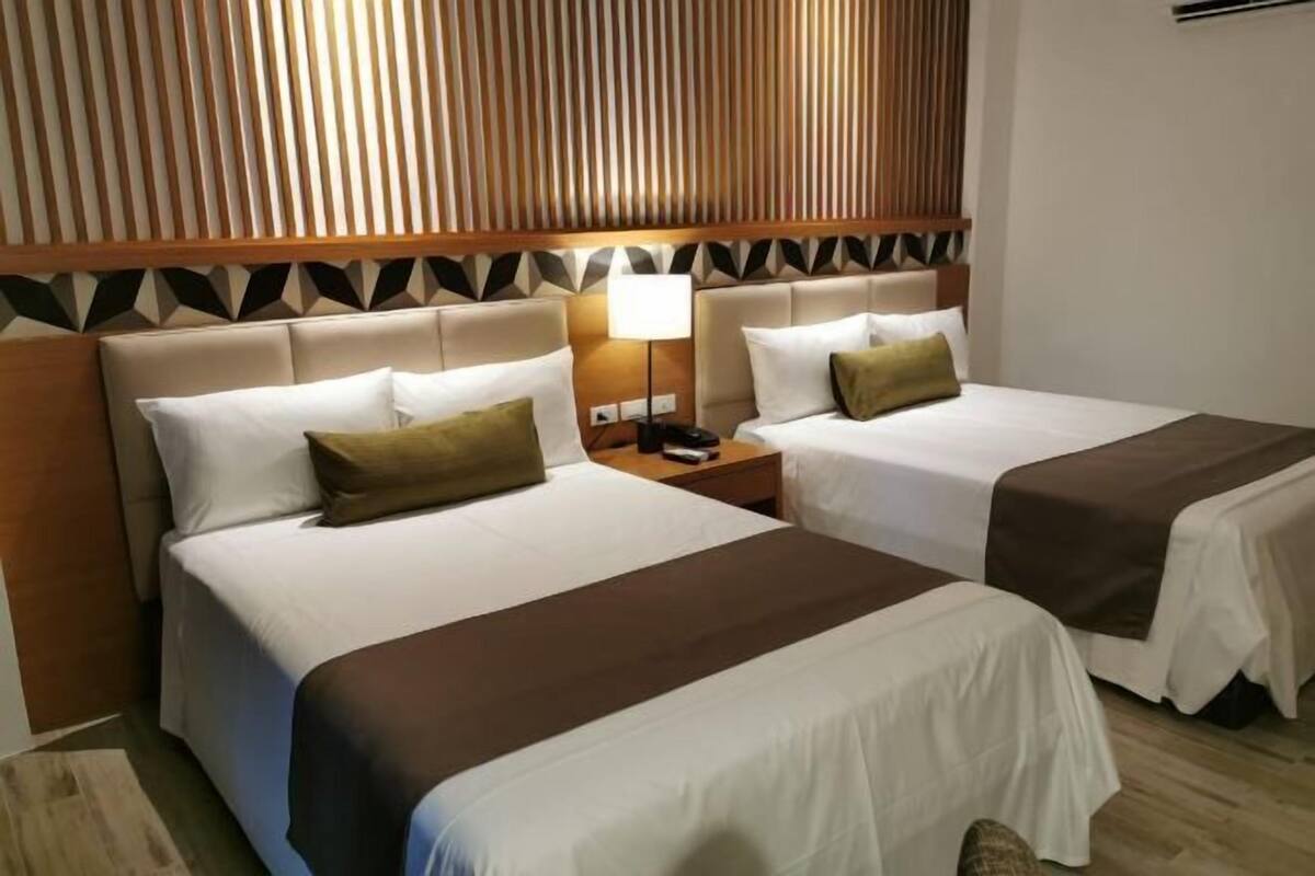 Ein Hotelzimmer mit zwei Betten, einem Nachttisch mit Lampe und einem hölzernen Kopfteil mit geometrischem Muster.